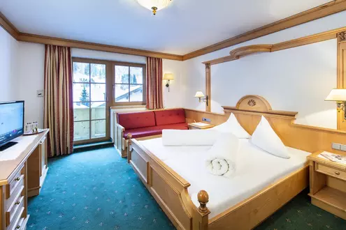 Hotelzimmer mit Balkon, Doppelbett aus Holz und Liegesofa mit rotem Polsterbezug