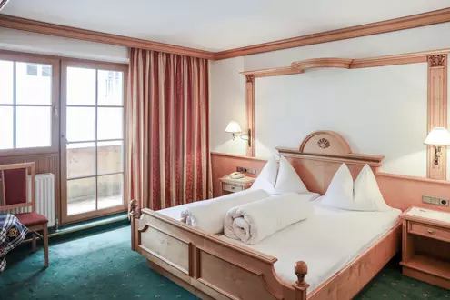 Hotelzimmer mit Balkon, Doppelbett und Nachttischen aus Holz und grünem Teppichboden