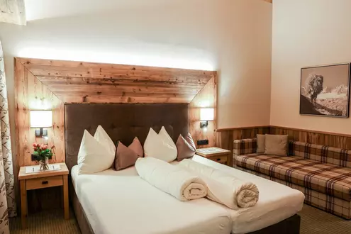 Doppelbett mit gepolstertem Kopfteil und Liegesofa in einem Hotelzimmer