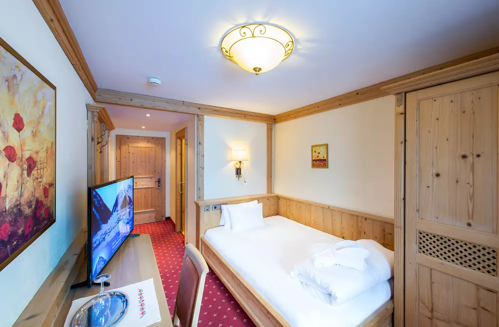 Hotelzimmer mit Einzelbett, Schreibtisch und Wandschrank aus Holz