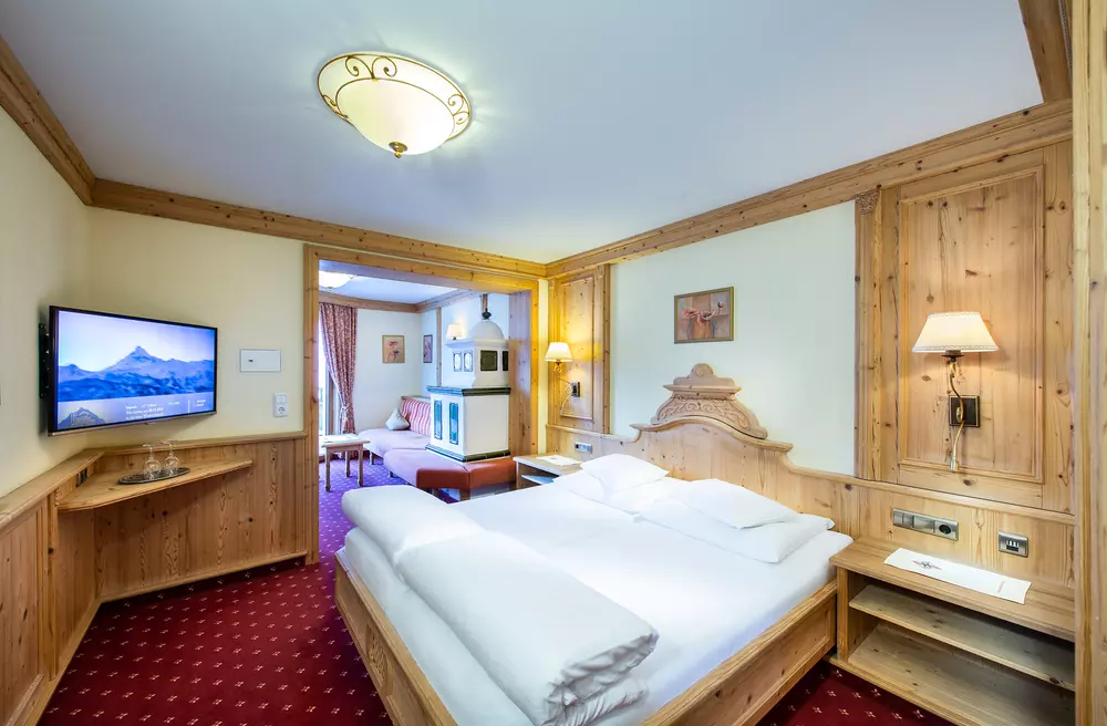 Hotelzimmer mit Doppelbett und gemütlicher Stube mit Kachelofen