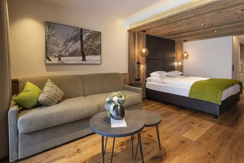 Doppelbett in einem modern eingerichteten Hotelzimmer mit Sofa und vertäfelter Wand