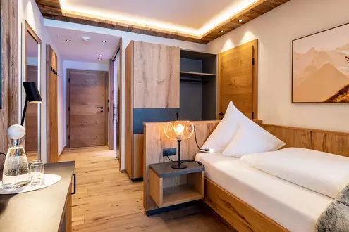Einzelbett in einem modern eingerichteten Hotelzimmer mit Parkett und Holzmöbeln
