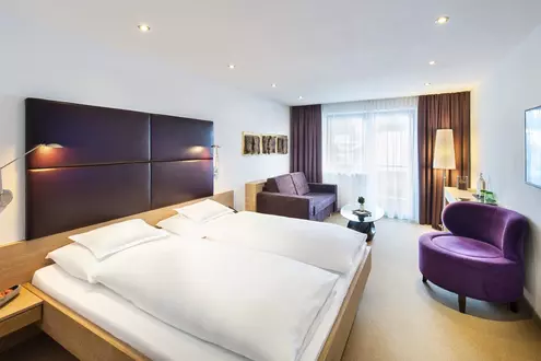 Doppelzimmer mit violetter Einrichtung, Fernseher und gemütlicher Sitzecke mit Sofa