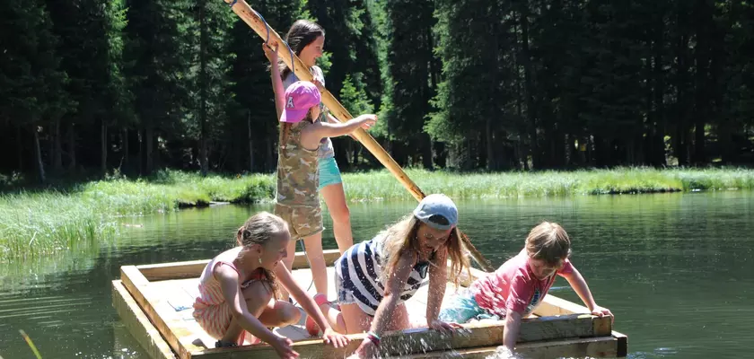 Kinder auf einem Floß aus Holz und einer Stake zum Paddeln in einem Waldsee im Sommer