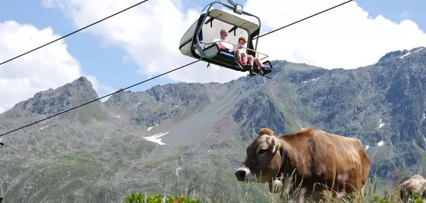Pärchen in einer Gondel auf einer Seilbahn und Kuh mit Kuhglocke in den Bergen im Sommer