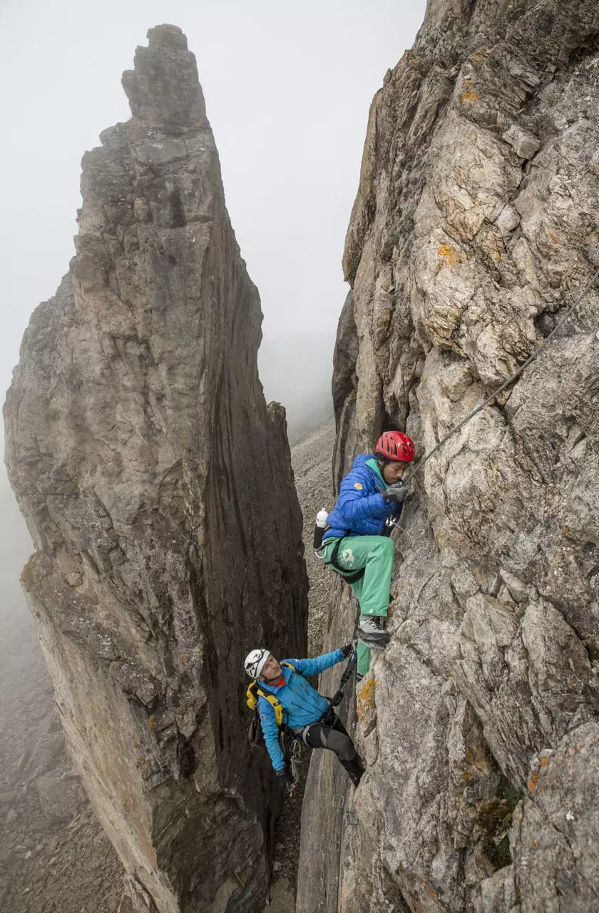 Männer mit Helm und Kletterseil in einer Felsspalte bei Nebel beim Klettern