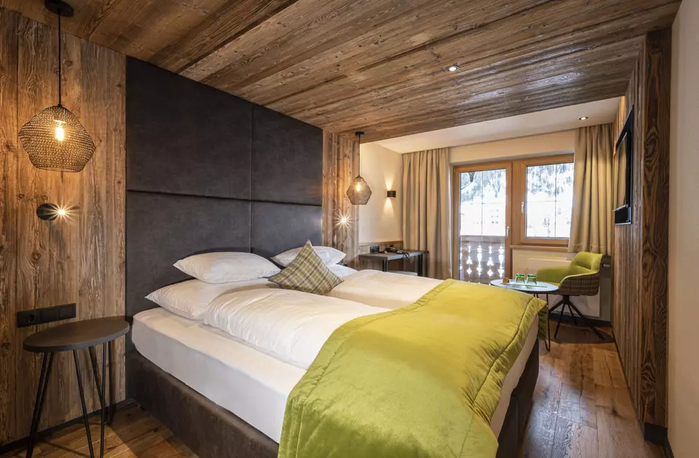 Doppelbett in einem modern eingerichteten Hotelzimmer mit Schreibtisch, Balkon und vertäfelter Wand