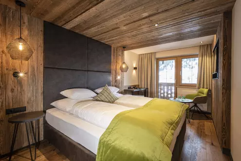 Doppelbett in einem modern eingerichteten Hotelzimmer mit Schreibtisch, Balkon und vertäfelter Wand