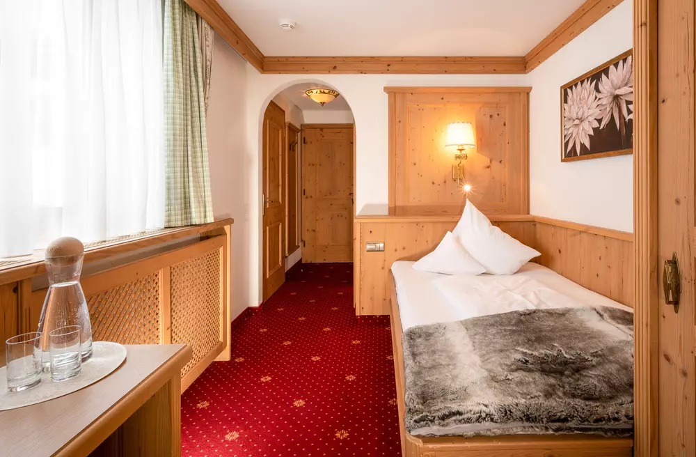 Einzelbett in einem schlichten Hotelzimmer mit rotem Teppich und Vertäfelung
