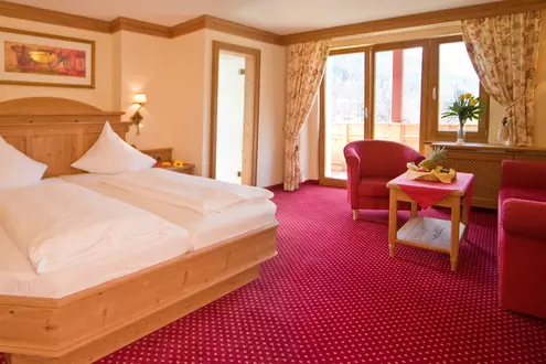 Hotelzimmer in roter Einrichtung mit Doppelbett, Sitzgruppe und Balkon