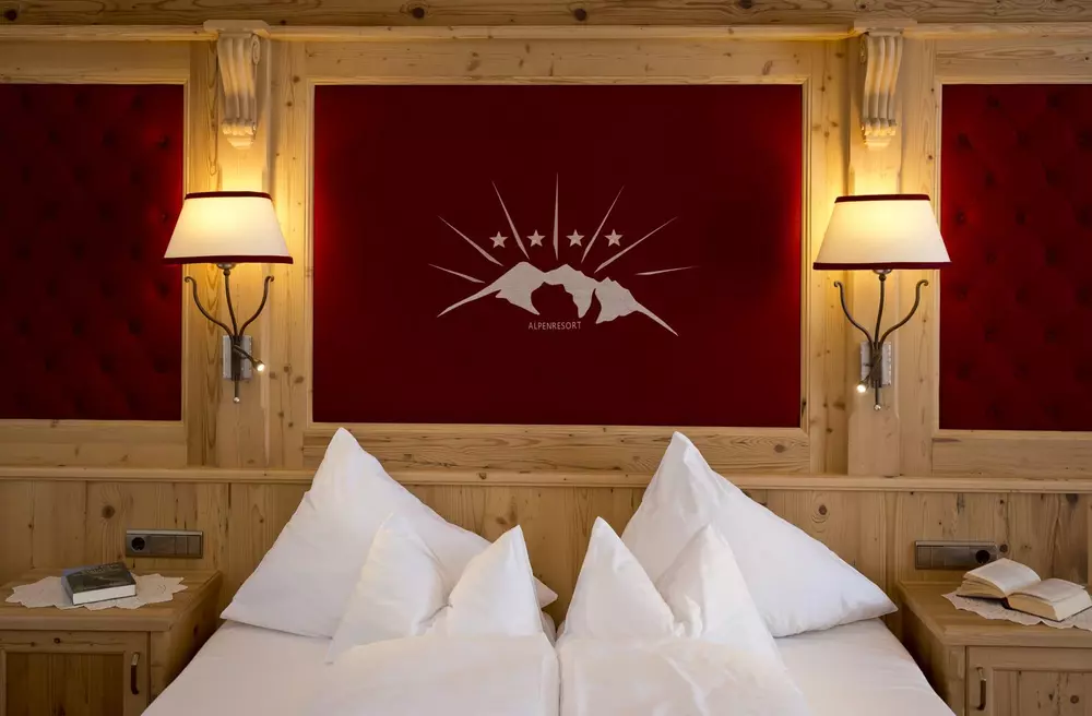 Doppelbett in einem rustikalen Zimmer im Alpenresort Fluchthorn mit vertäfelter Wand 