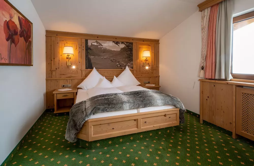Doppelbett in einem Hotelzimmer mit grünem Teppich und vertäfelter Wand